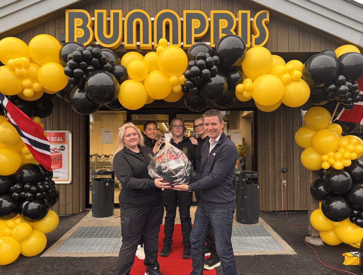 Kjøpmann Rita Winther Bue mottar gratulasjon fra AKAs prosjektansvarlig Even G. Skistad.  I bakgrunnen tre av ni ansatte, fv. Angelica, Linda og Lise Lotte.